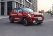 Беспроцентная рассрочка и льготный автокредит на Kia Sonet Prime - 3 Красный Kia Sonet Prime спереди сбоку на пустой улице между офисными зданиями