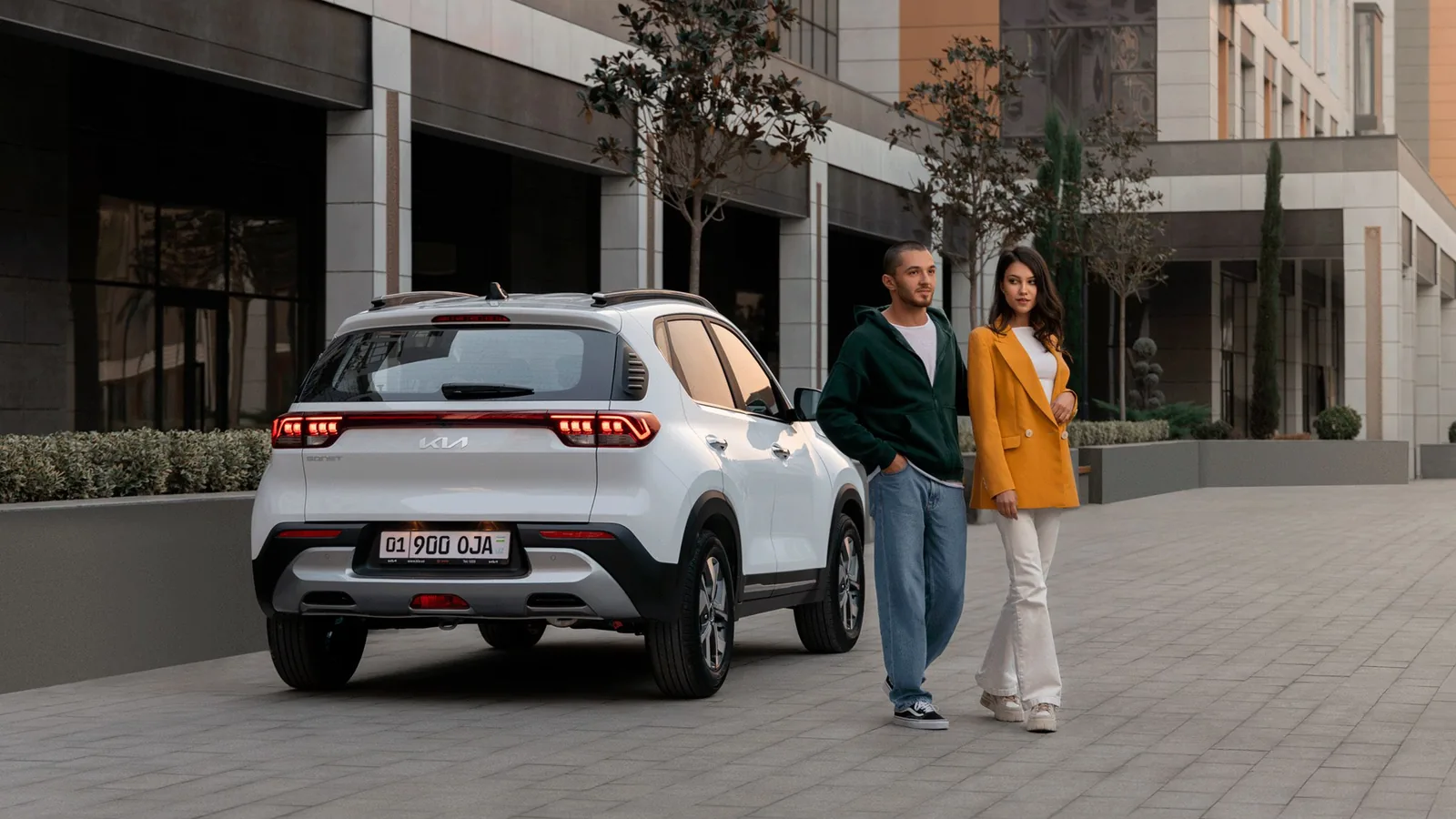 Kia Sonet в Узбекистане: цены, комплектации и характеристики - 1 Белый Kia Sonet сзади сбоку на городской улице, рядом идут парень и девушка