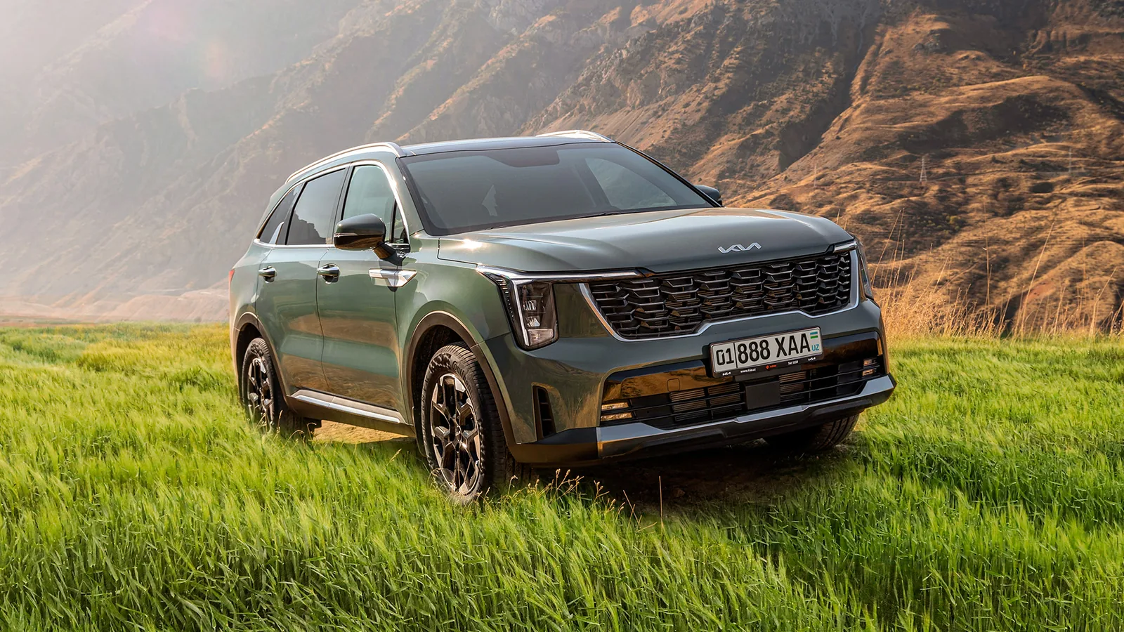 Kia Sorento в рассрочку без процентов: взнос и ежемесячный платеж - 1 Темно-зеленый Kia Sorento спереди сбоку в высокой траве на фоне гор