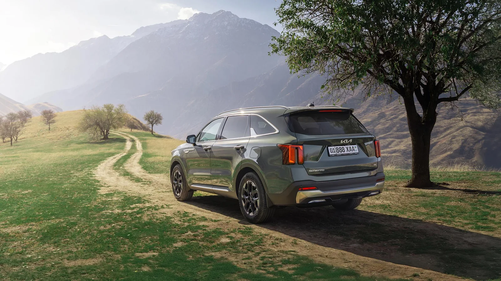 Kia Sorento в Узбекистане: цены, комплектации и характеристики - 1 Темно-зеленый Kia Sorento сзади сбоку на грунтовой дороге в горах рядом с деревом