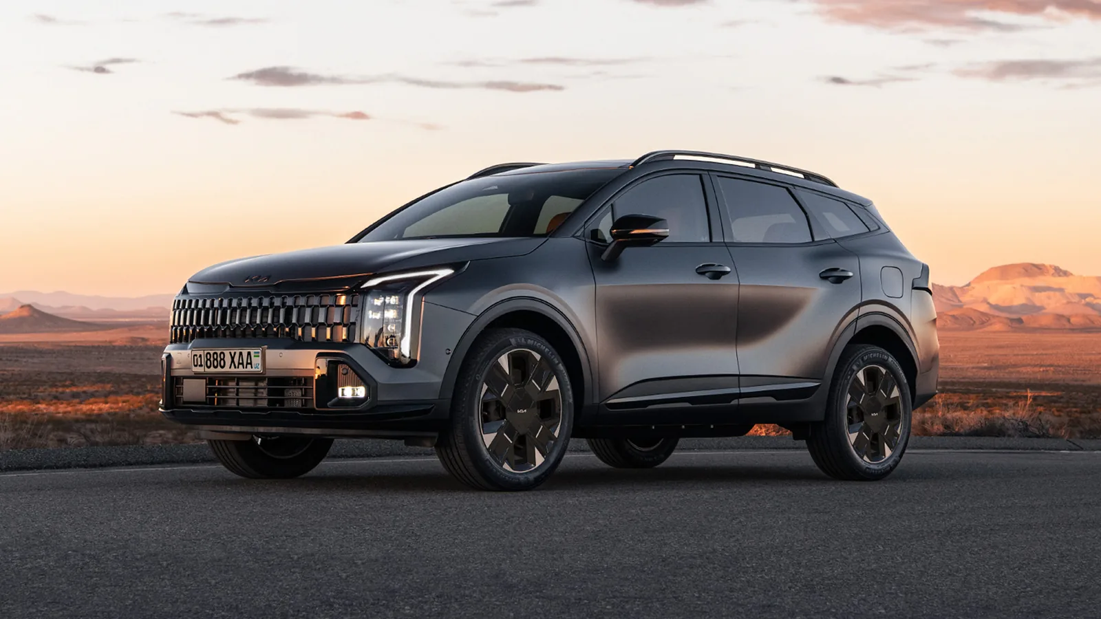 Kia Sportage в рассрочку без процентов: взнос и ежемесячный платеж - 1 Темно-серый обновленный Kia Sportage спереди сбоку на асфальте в пустыне на закате